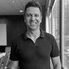 Black and white headshot of a man smiling while standing in a conference room with city view.