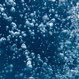 Close-up of underwater bubbles rising in clear blue water, representing purity in water analysis. 