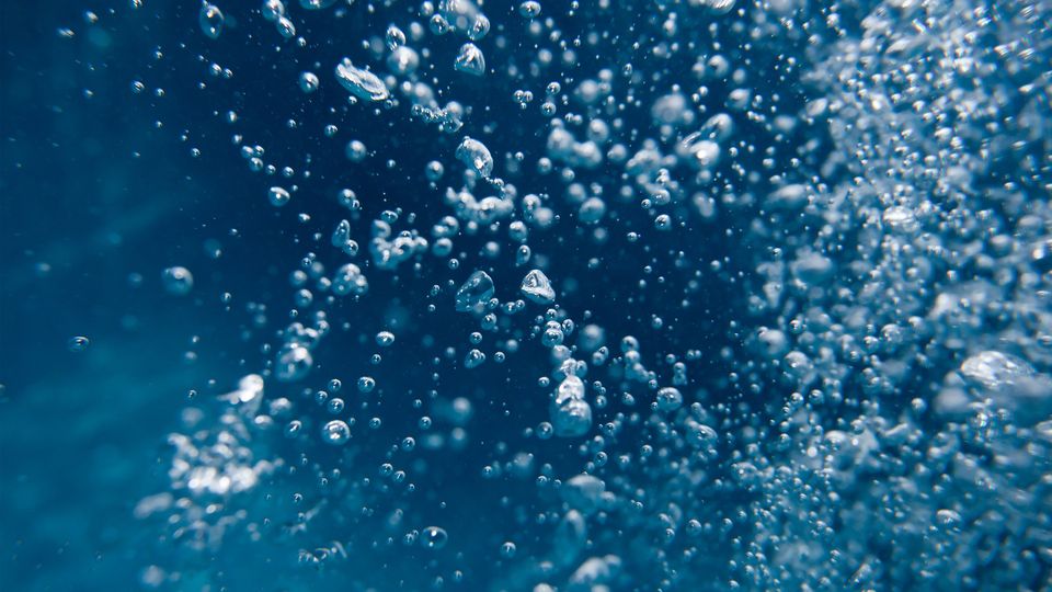 Close-up of underwater bubbles rising in clear blue water, representing purity in water analysis.