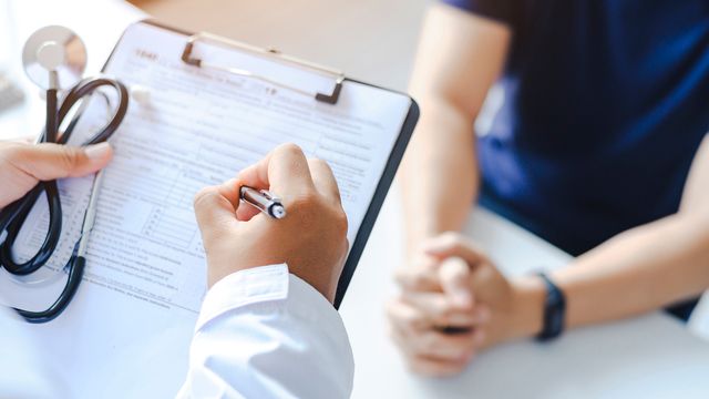A doctor holding a notepad and stethoscope prescribing medication to a male patient. 