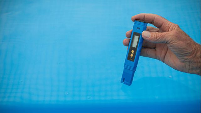Hand holding a digital pH meter to measure the water quality in a pool. 