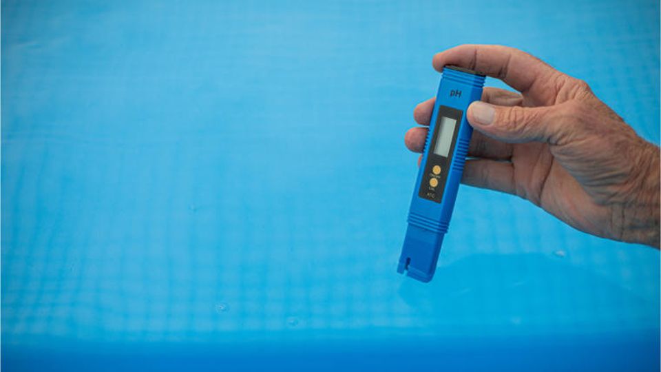 Hand holding a digital pH meter to measure the water quality in a pool.
