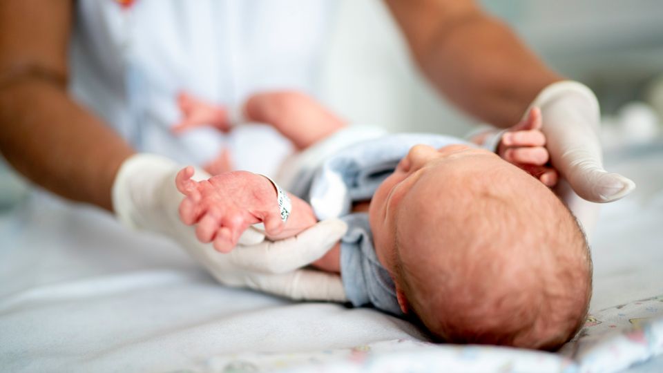 Medical professional gently handling a newborn baby, representing infant care and SIDS awareness.