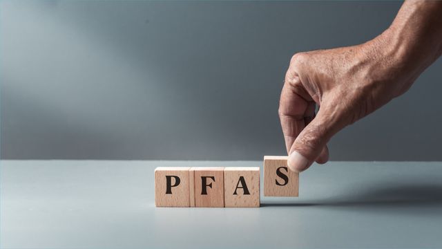 A person lining up four wooden blocks with letters on them to spell out "PFAS".  