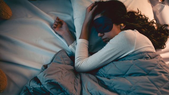 Woman sleeping with an eye mask and blanket in a dark bedroom. 