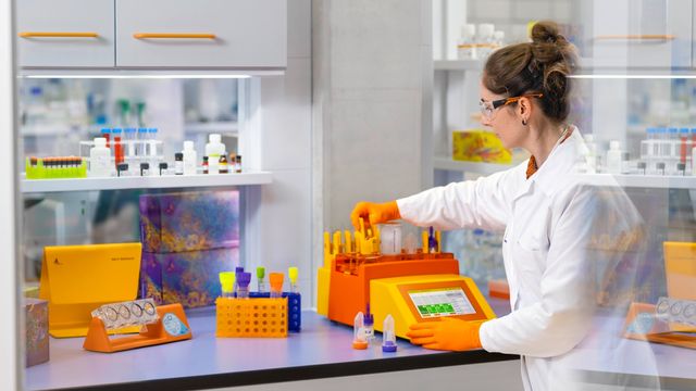 Scientist in a laboratory using the gentleMACS Octo tissue dissociator with heaters, wearing a lab coat, safety goggles, and orange gloves 