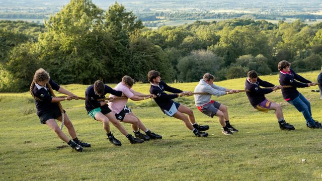 Group of people playing tug of war on a grassy hillside during an outdoor team competition. 