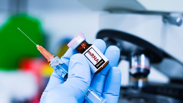 Syringe and vial of mRNA vaccine held in a gloved hand. 